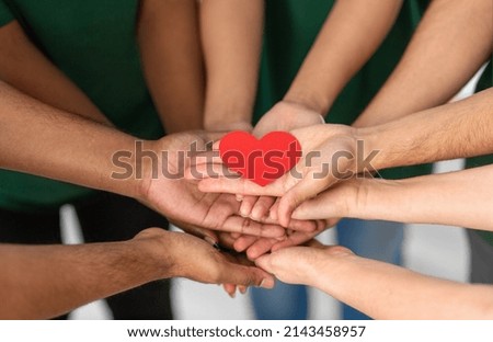 charity, support and volunteering concept - close up of volunteers's hands holding red heart at distribution or refugee assistance center
