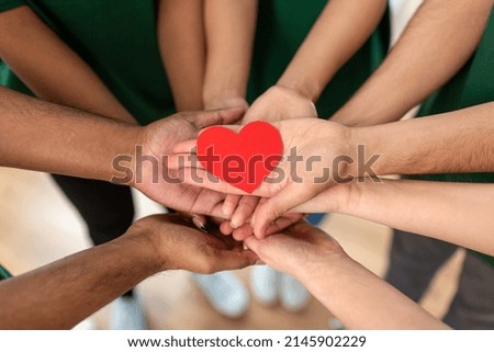 charity, support and volunteering concept - close up of volunteers's hands holding red heart at distribution or refugee assistance center