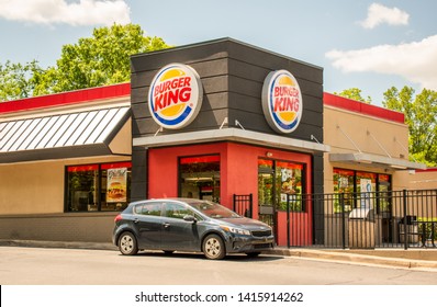 Charlotte, NC/USA - May 26, 2019: Exterior Long Shot Of Burger King Drive-in Fast Food Restaurant Showing A Vehicle At The Drive Through Window With Fenced In Patio Green Trees And Blue Sky And Clouds