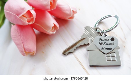 Charm Metal House And Heart Shaped Keychains, Engraved With Word HOME SWEET HOME, On Marble Table With Pink Flower. The Concept Of Warm Welcome To Customers For Real Estate Agent.