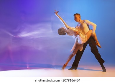 Charm. Young graceful dancers, flexible man and woman dancing ballroom dance isolated on gradient blue purple background in neon mixed light. Concept of art, timeless, beauty, music, style and ad