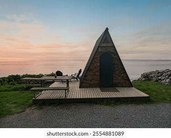 A charming A-frame cabin on a wooden deck overlooks the tranquil Strait of Juan de Fuca at sunset in Port Angeles, Washington, offering a serene coastal escape surrounded by natural beauty. - Powered by Shutterstock