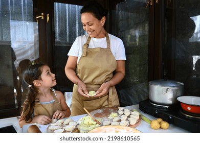 Charming African American Woman In Chef's Apron Admiring Her Cute Child, A Baby Girl Who Is Learning To Cook Dumplings Or Vareniki In A Summer Village Kitchen. Mother And Daughter Baking In Kitchen