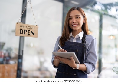 Charming Asian Businesswoman In An Apron Hold An Order Book In Front Of A Cafe Counter With A Beaming Smile Preparing To Open And Take Orders.