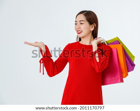 Charming Asian female buyer with shopping bags pointing aside on white background in studio and smiling at camera