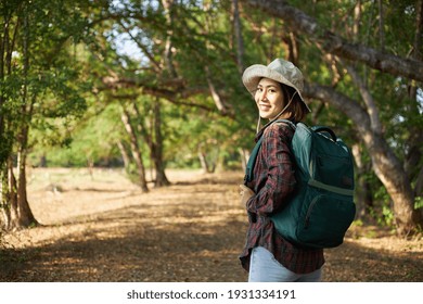 A Charming Asian Woman Carrying A Green Backpack And Wearing Casual Clothes Is Happily Wandering Through The National Park. Female Traveler Spends Their Vacations Going Hiking.