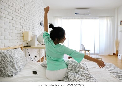 Charming Asian Woman Sit On Bed And Hand Up Wake Up On Morning In Simple White Room With Air Condition. Summer Season.