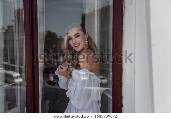 A charming beauty\
of the bride\'s Fashion pose at the window. Portrait of a modern\
bride through the window.