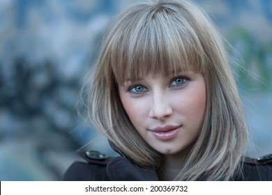 Charming Blond Haired Women Headshot Against Grungy Wall. Cute Blonde Girl Headshot In Grungy Settings. Young Women Portrait In Slums Front View. Solitude In The World