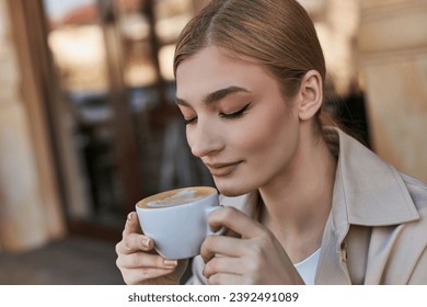 charming blonde woman in trench coat enjoying her cup of cappuccino in cafe, relaxed atmosphere - Powered by Shutterstock