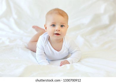 Charming blue-eyed 9 month old baby in white clothes on the bed