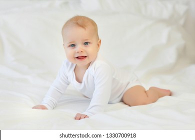 Charming blue-eyed 9 month old baby in white clothes on the bed