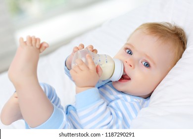 Em bé mắt xanh quyến rũ 7 tháng tuổi nằm trên giường và uống sữa từ chai
