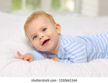 Charming blue-eyed baby 7 month old lying in bed in a striped bodysuit