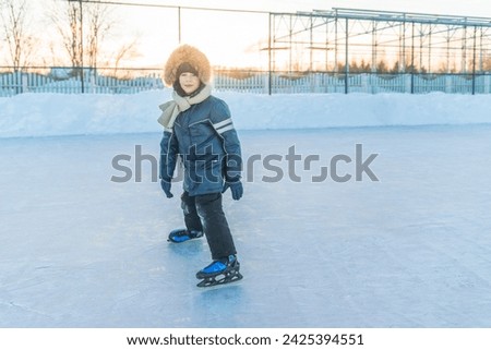 A charming boy in blue clothes learns to skate on a street skating rink.