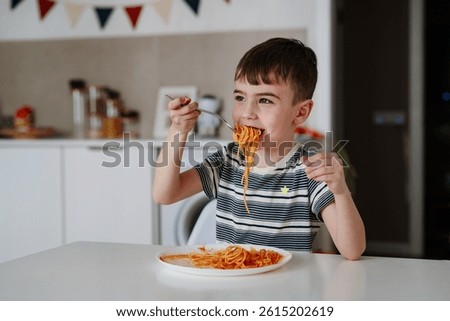 A charming boy eats spaghetti with tomato bolognese. A happy child eats freshly prepared healthy food indoors