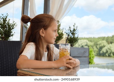 Charming brown-haired Caucasian girl enjoying refreshing delicious drink at a cafe gazing away at beautiful nature relaxing in the restaurant in hot summer holiday day - Powered by Shutterstock