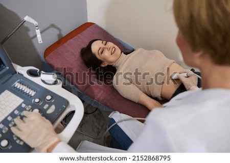 Charming Caucasian woman smiling at her attending doctor while checking her health during an ultrasound examination in a medical clinic. ultrasonography USG