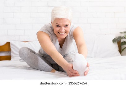 Charming Cheerful Mature Woman Stretching Her Legs And Doing Yoga In Her Bed. Waking Up And Morning Routine Concept