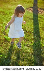 Charming Child In Linen Dress Walking On The Lawn