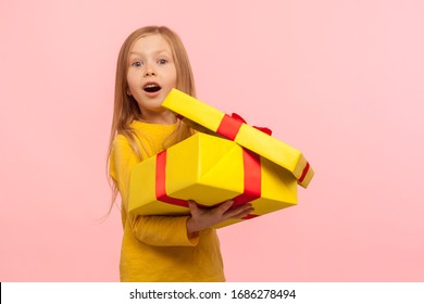 Charming Child Surprised By Birthday Present. Portrait Of Cute Little Girl Opening Gift Box And Keeping Mouth Open In Amazement, Shocked Expression. Indoor Studio Shot Isolated On Pink Background