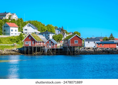 Charming coastal village in Norway with traditional red wooden cabins on stilts offer unique views of serene water and landscape. Reine, Lofoten, Norway - Powered by Shutterstock