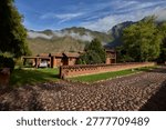 A charming cobblestone path leads to a serene Andean countryside retreat, where traditional adobe architecture blends seamlessly with lush gardens and the majestic mountain peaks rising through the morning clouds. The perfect escape from the rush of modern life, this tranquil highland sanctuary embodies the dream of peaceful retirement living — where slow mornings, clean mountain air, and timeless landscapes offer the ultimate reward for a life well lived.