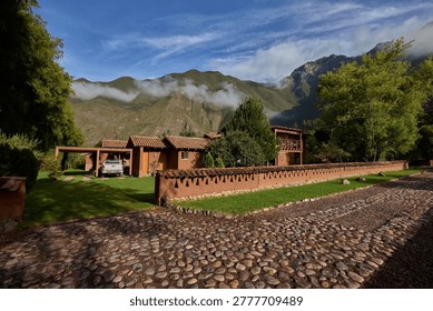 A charming cobblestone path leads to a serene Andean countryside retreat, where traditional adobe architecture blends seamlessly with lush gardens and the majestic mountain peaks rising through the morning clouds. The perfect escape from the rush of modern life, this tranquil highland sanctuary embodies the dream of peaceful retirement living — where slow mornings, clean mountain air, and timeless landscapes offer the ultimate reward for a life well lived.
