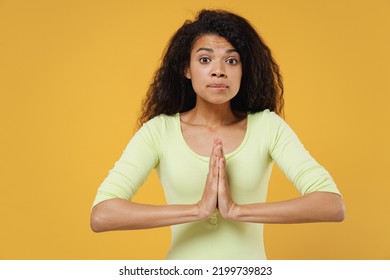 Charming Confused Sad Cute Fun Young Woman 20s Wears Green Shirt Hands Folded In Prayer Gesture Begging About Something Isolated On Yellow Background Studio Portrait. People Emotions Lifestyle Concept