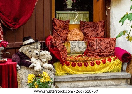 Charming café corner decoration featuring a large teddy bear wearing a hat and holding a smaller toy bear, surrounded by bright pillows and cozy, colorful fabrics.