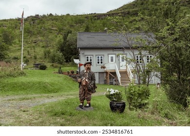 Charming Cottage in Lofoten Islands Showcasing a Whimsical Statue Amid Lush Greenery and Mountainous Backdrop - Powered by Shutterstock