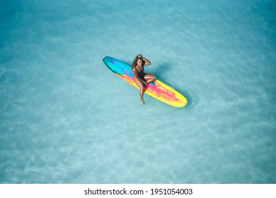 Charming curly African-American dark-skinned young woman, professional surfer sits on a long surfboard in the ocean, aerial shot from above  - Powered by Shutterstock