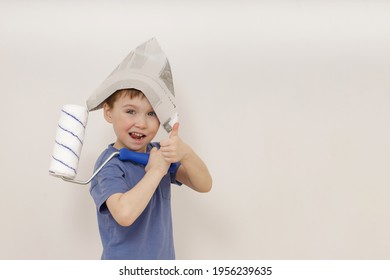 Charming Cute Little Emotional 5-year-old Boy In A Newspaper Hat Holds A White Roller In His Hand And Shows The Class . Concept Of Apartment House (renovation)