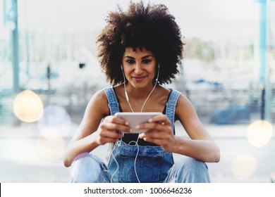 Charming Dark-skinned Girl With Afro Hair Watching Video On Mobile Phone Using Public Network Wifi Outside. Modern Female Entrepreneur Communicates Via Video Link With Her Personal Assistant