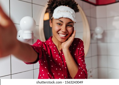 Charming dark-skinned woman in sleep mask is smiling, looking at camera and taking selfie - Powered by Shutterstock