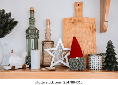 A charming display of holiday decorations on a wooden shelf features glass bottles, festive figurines, and a wooden cutting board. The atmosphere is warm and inviting, perfect for the season. - Powered by Shutterstock