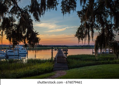 Charming Dock Over The Marsh And Water In Savannah, Georgia Framed By Hanging Spanish Moss During Sunrise