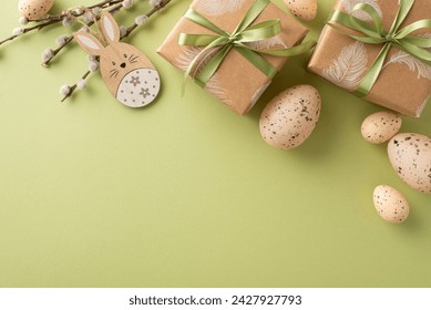 Charming Easter display idea. Overhead shot featuring brown kraft gift boxes, wooden Easter rabbit, speckled quail eggs, and fresh pussy willow branches, laid out on green surface with space for copy - Powered by Shutterstock