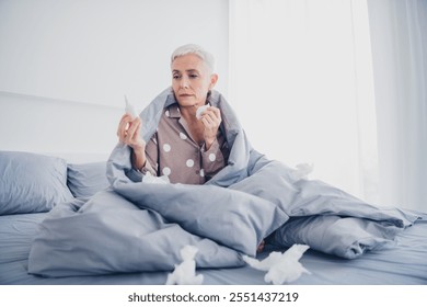 Charming elderly woman with white hair sitting in bed holding tissues, wearing pajamas, reflecting natural daylight - Powered by Shutterstock