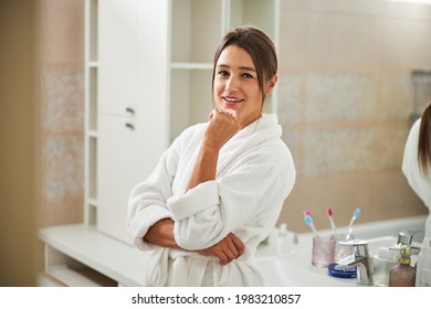 Charming Elegant Female In Plush Robe Holding Hand Under The Chin In Bathroom