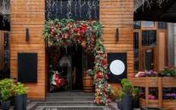 A Charming Entrance To A Wooden Building Adorned With Vibrant Red And Green Floral Arrangements, Indicating Spring Or Summer. A Classic Scooter Rests By The Doorway