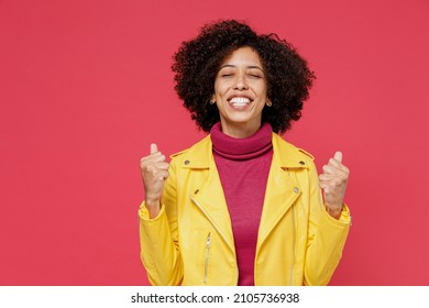 Charming Excited Fun Young Curly Black Latin Woman 20s Years Old Wears Yellow Jacket Eyes Closed Doing Winner Gesture Celebrate Clenching Fists Say Yes Isolated On Plain Red Background Studio Portrait