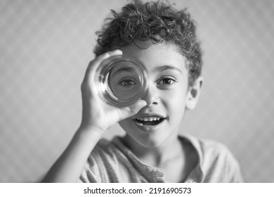 charming fair-skinned curly-haired boy plays with a glass imagining that it is a spyglass or a magnifying glass