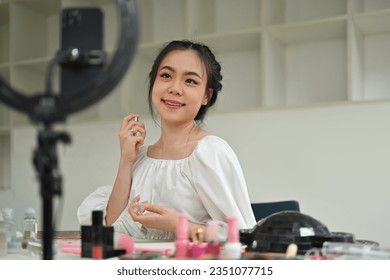 Charming female beauty blogger spraying perfume on her neck while recording video in dressing room. - Powered by Shutterstock