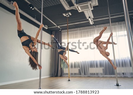 Charming female dancers in gymnastics clothes doing acrobatic tricks while dancing on pylons in studio
