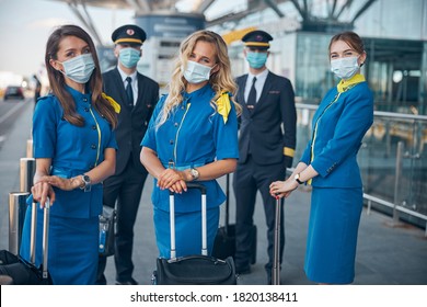 Charming Flight Attendants And Pilots In Protective Face Masks Waiting For Flight At Airport