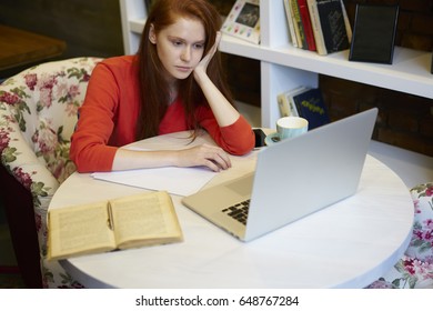 Charming Foxy Tired Teen Student Watching Training Webinar On Modern Laptop Computer Connected To Wireless Internet While Preparing For Upcoming Examination Sitting In Comfortable Coworking Space