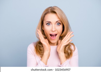 Charming, funny, pretty, comic, attractive, shocked woman with open mouth, screaming, shouting, yelling over grey background, holding palms near cheeks