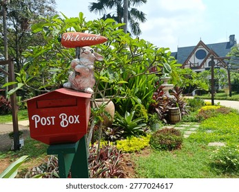 Charming garden scene featuring a decorative red post box with a cute rabbit statue holding a “Welcome