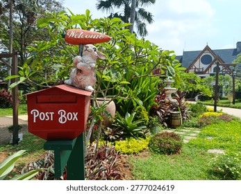 Charming garden scene featuring a decorative red post box with a cute rabbit statue holding a “Welcome
